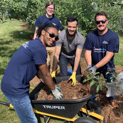 Four Boston Scientific employees in t-shirts and work gloves reach into a wheelbarrow of mulch as they work to improve the health of communities and the planet.