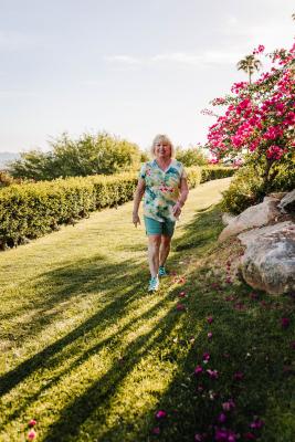 An older white woman, dressed in a floral shirt, smiles as she walks through a garden after her successful Vertiflex Procedure.