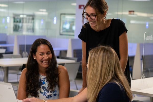 Three women - two sitting, one standing - share a big smile, knowing that their generous Boston Scientific employee benefits make it a Best Place to Work.