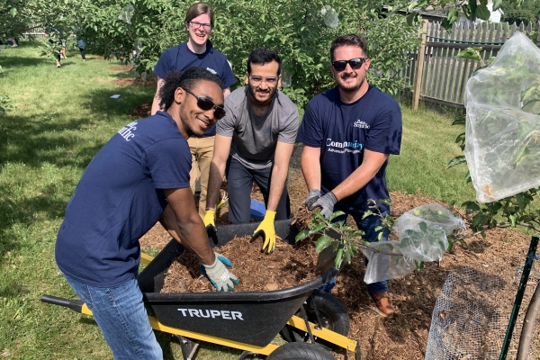 Four Boston Scientific employees in t-shirts and work gloves reach into a wheelbarrow of mulch as they work to improve the health of communities and the planet.