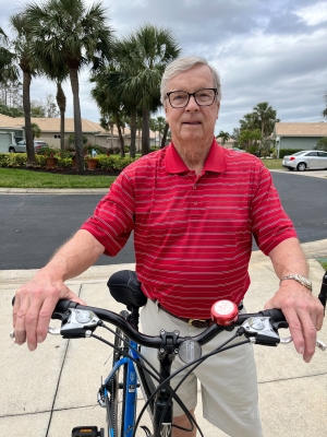 Randy, a white man with glasses and grey hair, stands next to his bicycle, which he can ride again after undergoing the Vertiflex procedure.