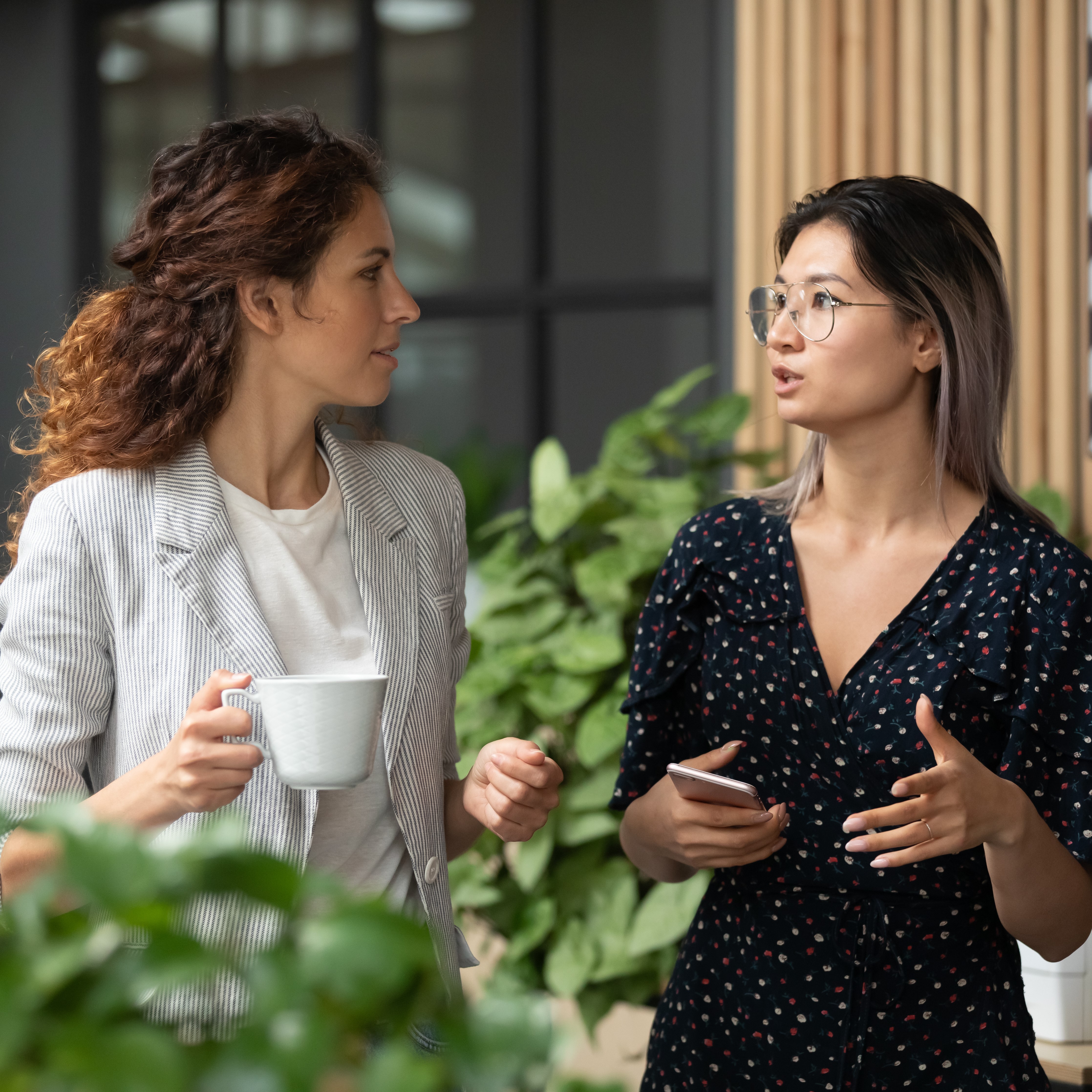 Two women, one white and one Asian, chat while on a coffee break from work, where they help to build a culture of equity.
